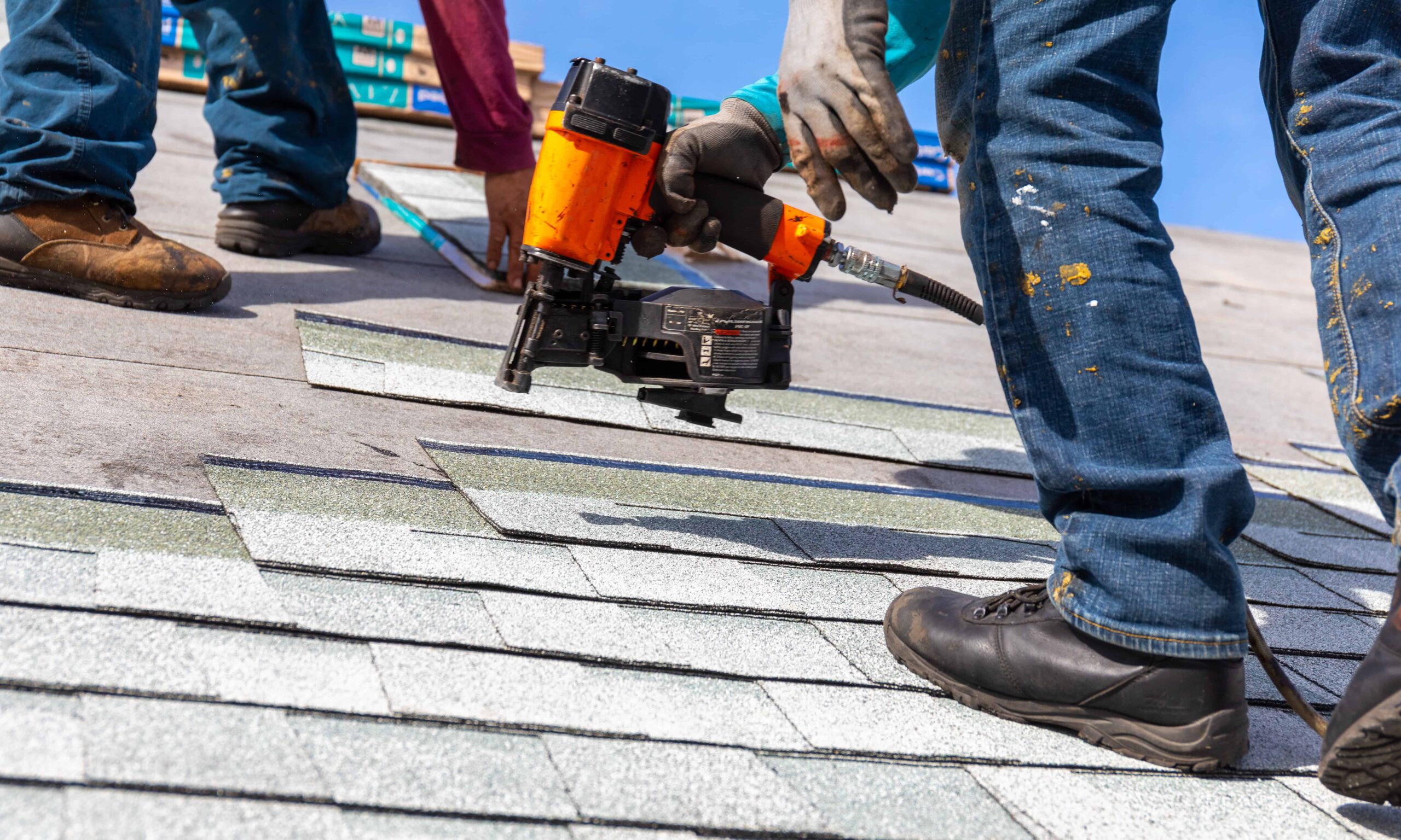 A contractor nailing a roof shingle with an orange nail gun