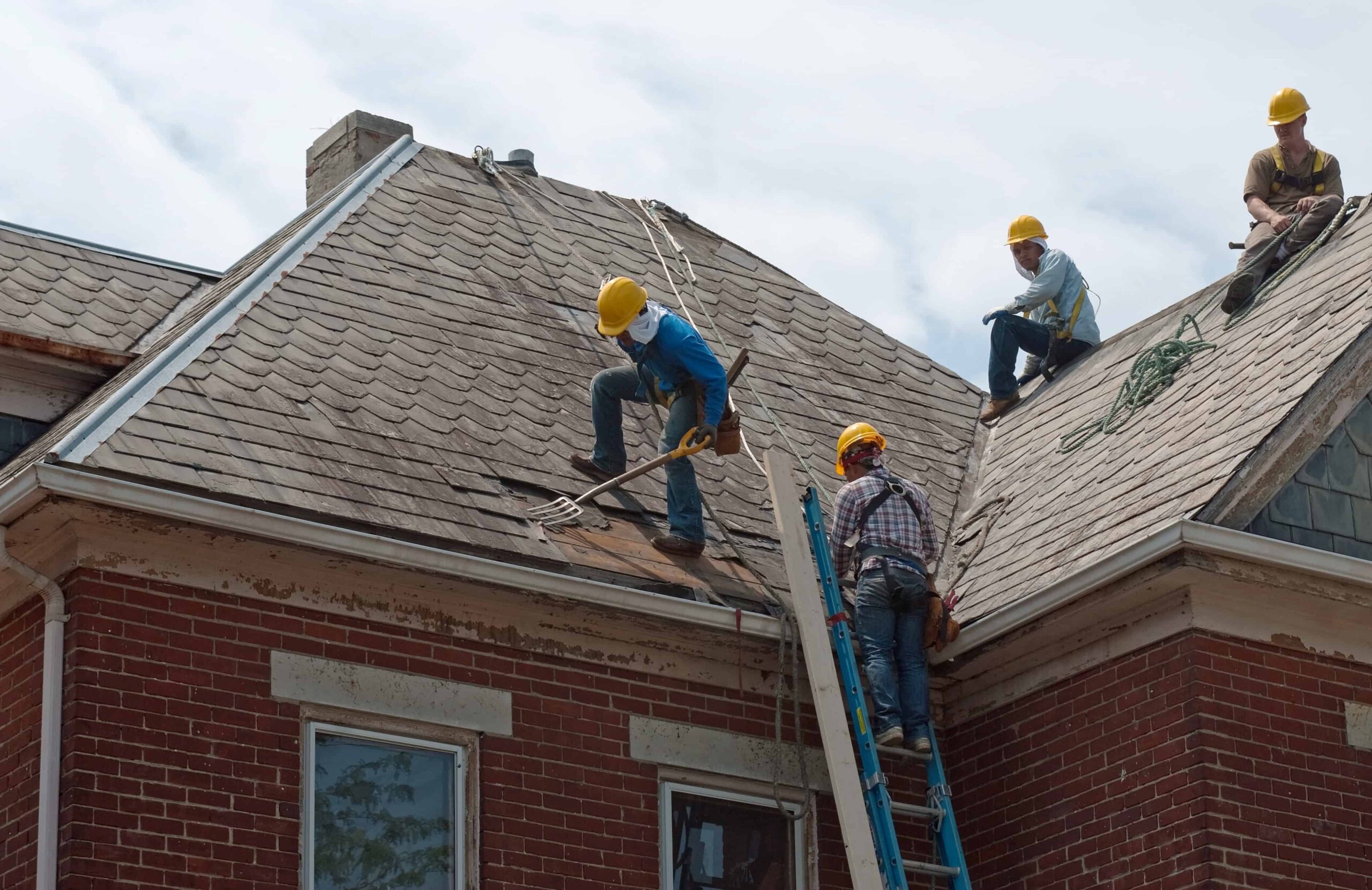 roofing contractors wearing yellow hard hats working on a roof