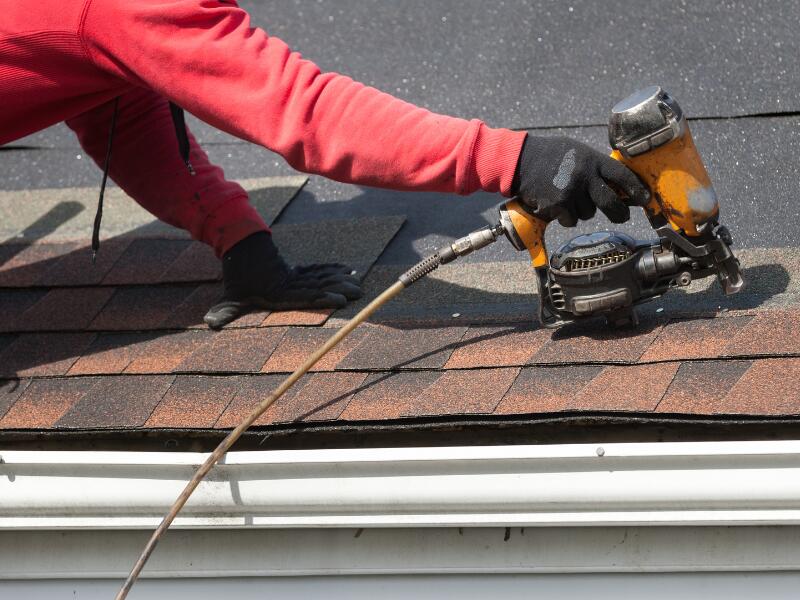 A roofer drilling on a roof shingle.